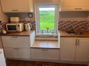 斯莱戈Daffodil Lodge的厨房配有白色橱柜、水槽和窗户。