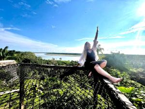 Puerto NariñoReserva Natural Natura Park的坐在栅栏顶部的女人,手臂在空中