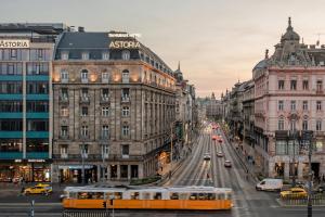布达佩斯阿斯托瑞亚市中心丹比乌斯酒店的一辆黄色的巴士驶向城市街道,街道上有许多建筑