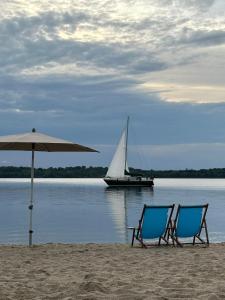莱比锡Leipzig-Südwest的海滩上的两把椅子和一把遮阳伞,带帆船