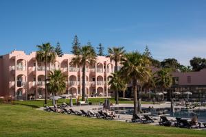 阿尔布费拉Vila Gale Collection Praia的一座大型粉红色建筑,种植了棕榈树,设有游泳池