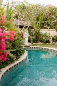登巴萨Villa Nelayan Sands的一座游泳池,旁边是一些花卉,旁边是雕像
