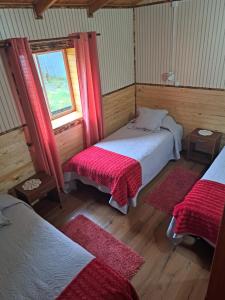 普尤瓦比港Cabañas Robinson的客房设有两张床和一个带红色窗帘的窗户。