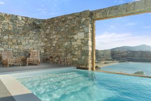 凯勒里瓦迪Radisson Blu Euphoria Resort, Mykonos的一个带两把椅子和石墙的游泳池