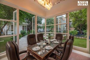 新德里StayVista's Indraj Manor - Roman-Inspired Villa with Posh Interiors, Mesmerizing Garden & Outdoor Fireplace的一间带桌椅和窗户的用餐室