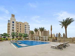 迪拜StoneTree - Elegant 1 BR in Madinat Jumeirah Living Rahaal 2的一座带椅子和棕榈树的游泳池以及建筑