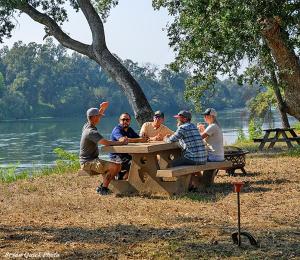 雷丁Three Bedroom River Access的一群坐在湖畔野餐桌上的人