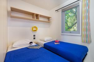 格雷乌莱班Camping Paradis La Pinede的带窗户的客房内的两张床和蓝色床单