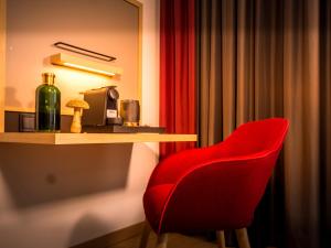 日内瓦IntercityHotel Geneva的一张红椅,坐在桌子旁,放一瓶葡萄酒