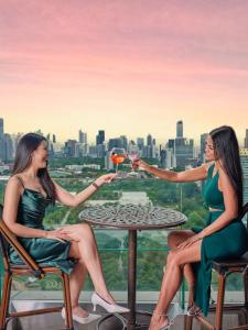 曼谷Column Bangkok Hotel的两个女人坐在桌子边,喝一杯酒