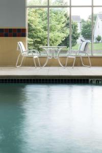 利伯蒂堪萨斯城利伯蒂希尔顿恒庭酒店的游泳池旁的三把椅子和一张桌子