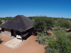 Gobabis西巢小屋旅馆的停泊在有稻草屋顶的建筑物中的汽车