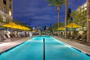 安纳海姆Hilton Garden Inn Anaheim Resort的游泳池在晚上提供椅子和遮阳伞