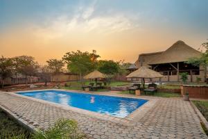 利文斯顿The Nkhosi Livingstone Lodge and Spa的一座带桌子和遮阳伞的游泳池,位于一座建筑旁边