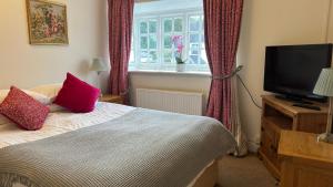 温彻斯特The Cricketers Inn的一间卧室配有一张带红色枕头的床和电视。