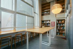 福冈Common de - Hostel & Bar的图书馆里的桌子,椅子和大窗户