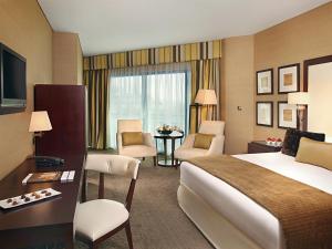 迪拜Mövenpick Grand Al Bustan的酒店客房,配有一张床、一张桌子和椅子