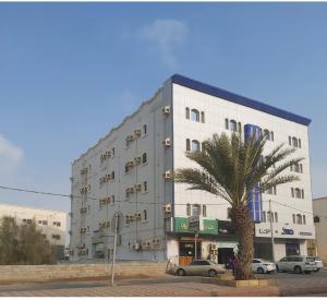 Al Qunfudhahاجنحة ارمادا的一座白色的大建筑,前面有一棵棕榈树