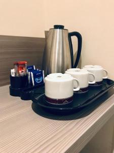 新德里Qotel Hotel Ashok Vihar Couple Friendly的盘子,盘子上放着三个咖啡杯和一个水壶