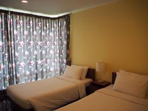 华欣Baan Sanploen. Unit 244的一间卧室设有两张床和一个带花卉窗帘的窗户。
