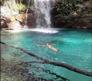 戈亚斯州上帕莱索Villa de Assis Suítes的在瀑布前的游泳池游泳的人