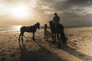 帕杰Kinazi Upepo Beach Eco Lodge的一名男子和一名女子在海滩上骑马