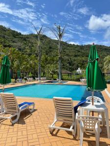 弗洛里亚诺波利斯Canto da Ilha的一个带两把草坪椅和绿伞的游泳池