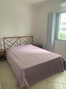 瓜鲁雅Apartamento Astúrias a menos de 50m da praia的一间卧室配有一张带紫色床罩的床和窗户。