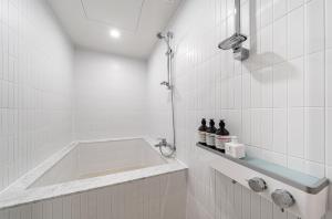 丽水市Browndot Hotel Yeosu Yeocheon的白色瓷砖浴室内的浴缸