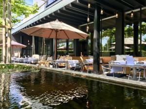 圣尼古拉赛维尔酒店的池塘旁的餐厅,配有桌子和遮阳伞