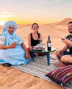 梅尔祖卡Overnight Desert Camp的一群坐在沙漠里的人,戴着酒杯