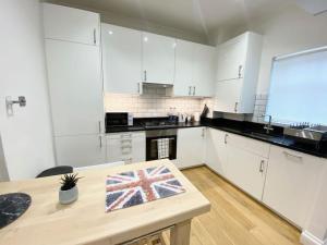 伦敦2 Bedroom Flat in Whitechapel!的厨房配有白色橱柜和一张带旗帜的桌子