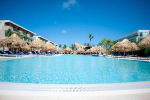 蓬塔卡纳Serenade All Suites - Adults Only Resort的一个带稻草遮阳伞和椅子的大型游泳池