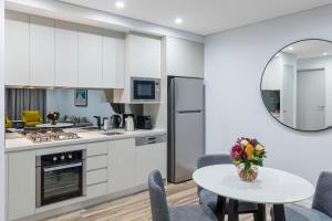 悉尼邦迪交界处美利通公寓式酒店的厨房配有白色橱柜和桌椅
