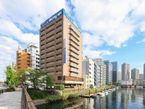 东京多美迎东京八丁堀酒店的一座高大的建筑,毗邻一条有建筑物的河流