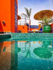 马拉喀什Riad Le Jardin de Lea, Suites & Spa的一座带橙色建筑和遮阳伞的游泳池