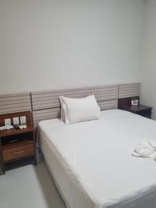 帕劳阿佩巴斯Carajas Hotel的卧室配有一张白色的大床和床头柜。