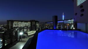 约翰内斯堡ANEW Hotel Parktonian Johannesburg的夜间在建筑物屋顶上的游泳池