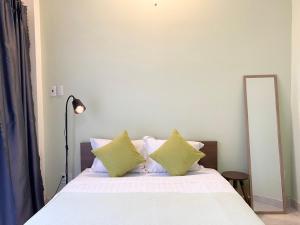 胡志明市Acorn Saigon Hotel - Bui Vien的一张带白色床单和绿色枕头的床,旁边是镜子