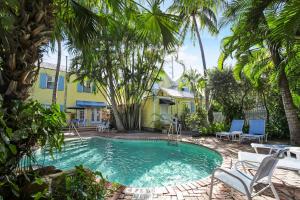 基韦斯特Tranquillity Guest House的棕榈树黄色房子前面的游泳池
