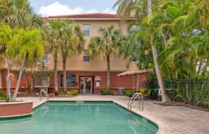 帕诺滩Extended Stay America Premier Suites - Fort Lauderdale - Cypress Creek - Park North的棕榈树建筑前的游泳池