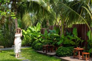 会安Shining Riverside Hoi An Boutique & Spa的站在花园中的戴帽子的女人