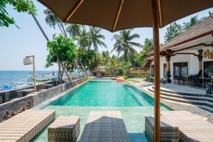 新加拉惹Bali Taoka Beach Villa的毗邻大海的带遮阳伞的游泳池