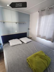 纳博讷Mobil-home cosy 166的一间卧室配有带两个枕头的床和窗户