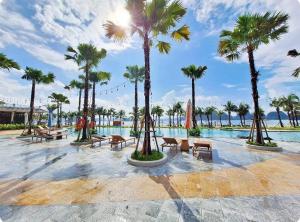 Royal Villa Vân Đồn Quảng Ninh的一个带棕榈树和长椅的游泳池的度假酒店