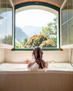 迈尔霍芬Sylvana's Wohlfühl Hotel的坐在浴缸里,看着窗外的女人