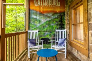 加特林堡SmokiesBoutiqueCabins would love to host you! 4 miles to Gatlinburg Strip! Resort Pool open May 1 through Oct 1! Views, Shuffleboard, Hot Tub, Arcade!的门廊上的两把椅子和一张桌子