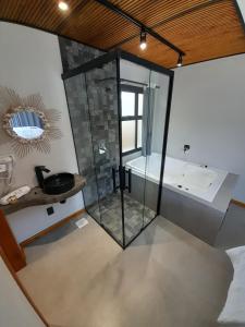 普腊亚罗萨Pousada Kirana的一间带玻璃淋浴和浴缸的浴室