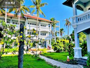 Ấp Thiện SơnHANZ Sun Sea Glamping & Beach Resort的一座白色的大建筑,前面有一棵棕榈树