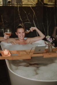 阿尔努埃罗VIBE LUXURY CABINS的浴缸里的女人,手提电脑和一杯葡萄酒